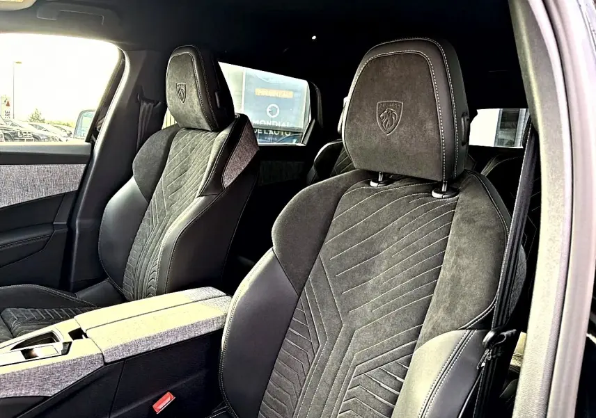 Vue intérieure des sièges avant noirs en cuir et alcantara du Peugeot 5008 Hybrid 145 GT, avec logo Peugeot brodé sur les appuis-tête.