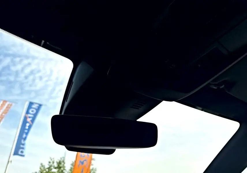 Vue intérieure du pare-brise et du rétroviseur central d'un Peugeot 5008 noir, avec ciel et drapeaux en arrière-plan.