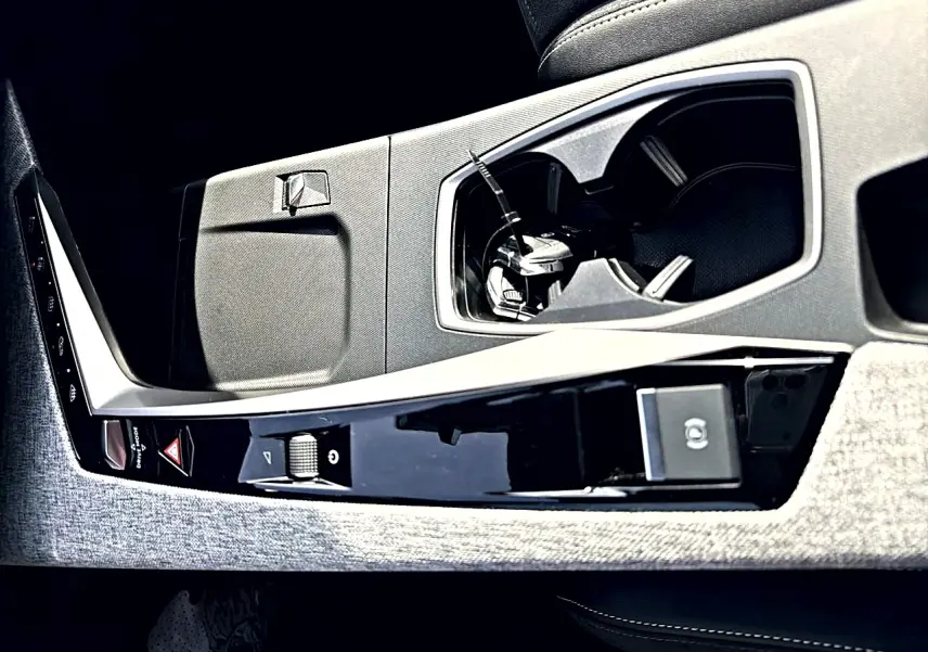 Détail de la console centrale intérieure du Peugeot 5008 Hybrid 145 GT e-dcs6 2025, avec porte-gobelets et commandes noires.