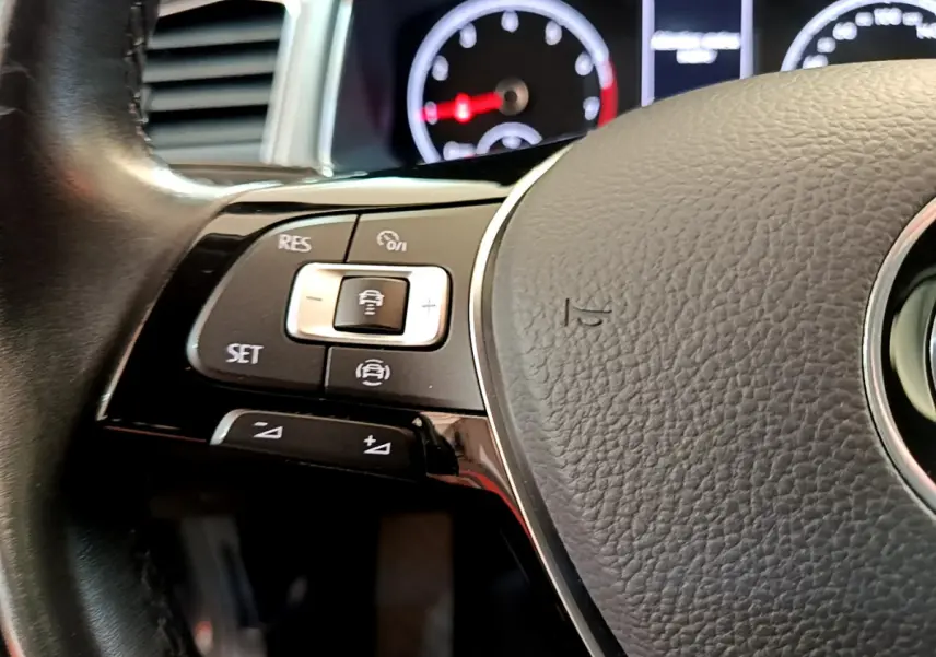 Gros plan sur les commandes du volant cuir noir du Volkswagen T-Roc 2021, avec tableau de bord numérique en arrière-plan flou.