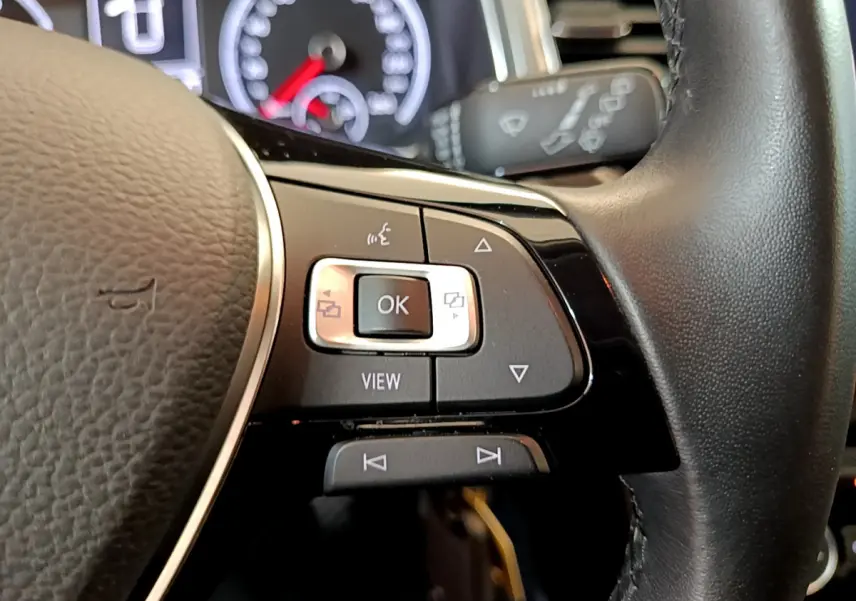 Gros plan sur les commandes au volant côté gauche du Volkswagen T-Roc gris foncé, avec tableau de bord en arrière-plan.