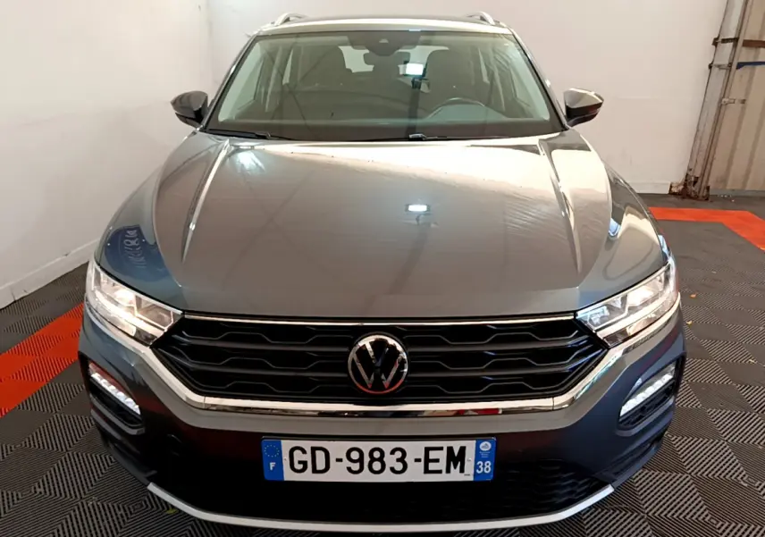 Vue avant d'un Volkswagen T-Roc gris foncé avec calandre noire et phares LED allumés dans un garage.