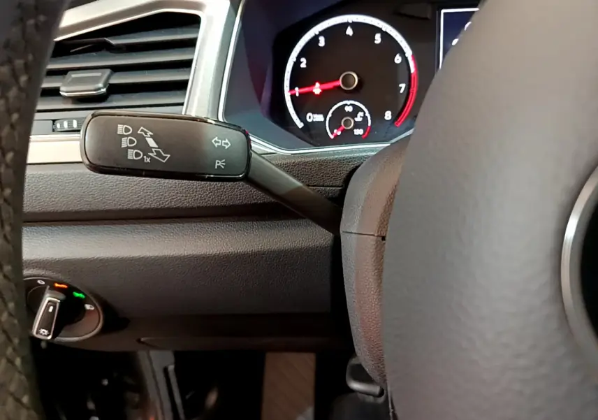 Détail intérieur du volant et levier de clignotant du Volkswagen T-Roc gris foncé, avec tableau de bord numérique visible.