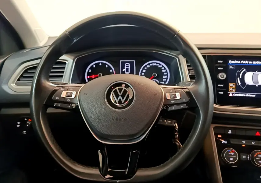 Vue intérieure centrée sur le volant cuir noir du Volkswagen T-Roc avec tableau de bord et écran tactile allumés.