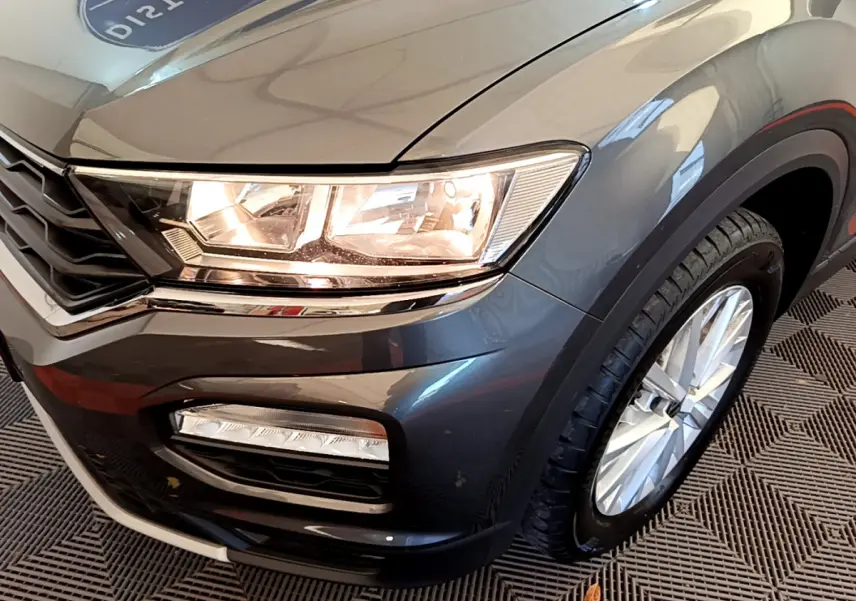 Gros plan sur l'avant droit d'un Volkswagen T-Roc gris foncé, mettant en valeur le phare et la roue.