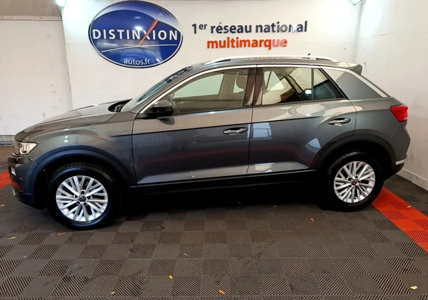 Vue de profil côté gauche d'un Volkswagen T-Roc gris foncé stationné en intérieur avec jantes argentées.