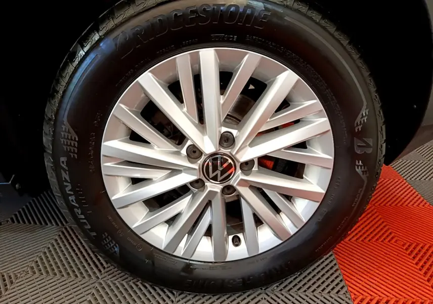 Gros plan sur la jante argentée avec logo Volkswagen du Volkswagen T-Roc gris foncé, pneu Bridgestone visible.