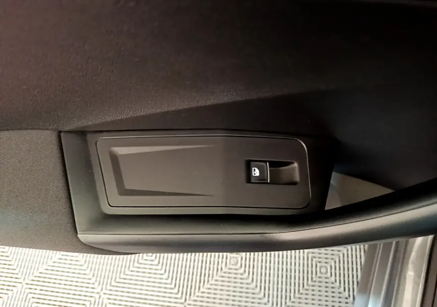 Gros plan sur le bouton d'ouverture de coffre intégré à la garniture intérieure de porte côté conducteur du Volkswagen T-Roc gris foncé.