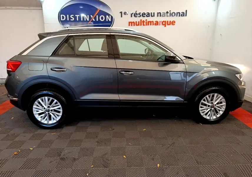 Volkswagen T-Roc gris foncé vue de profil côté gauche, avec jantes alliage et barres de toit noires.