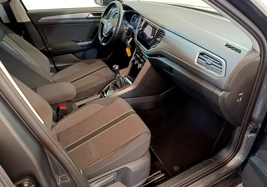 Vue intérieure côté passager du Volkswagen T-Roc gris foncé, montrant tableau de bord et sièges tissu avec console centrale.