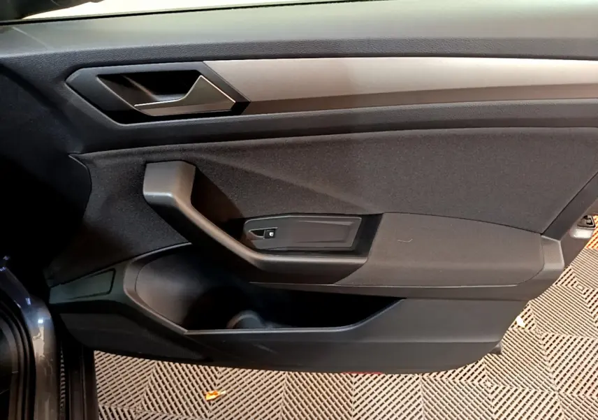 Vue intérieure du panneau de porte côté conducteur du Volkswagen T-Roc gris foncé, avec poignée et commande de vitre électrique.