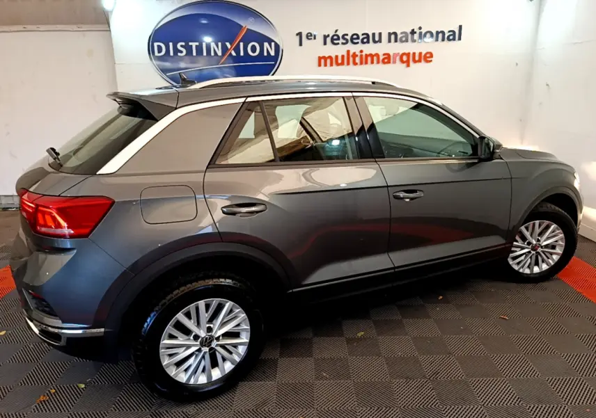Vue latérale droite d'un Volkswagen T-Roc gris foncé avec toit blanc et jantes alliage en intérieur showroom.