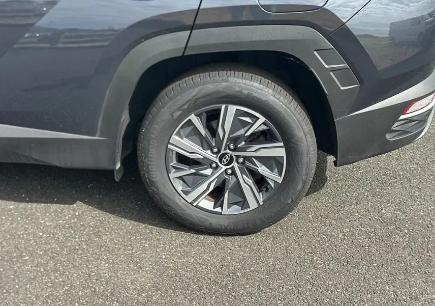Gros plan sur la roue arrière droite d’un Hyundai Tucson gris 2023, soulignant la jante en alliage au design géométrique.