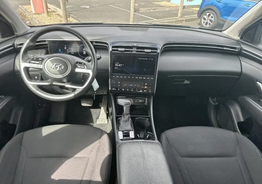 Vue intérieure avant du Hyundai Tucson 2023 gris, montrant le tableau de bord, volant multifonction et console centrale avec écran tactile.