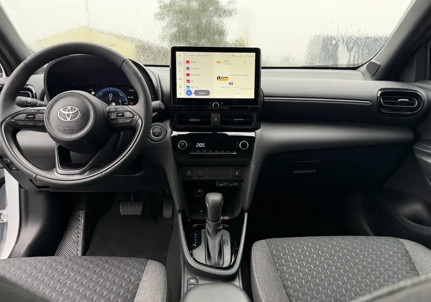 Vue frontale de l'habitacle de la Toyota Yaris Cross blanche, montrant le volant, l'écran tactile et la console centrale moderne.