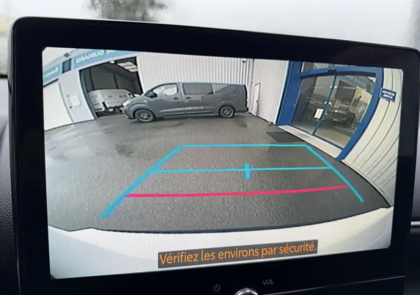 Vue caméra de recul d'une Toyota Yaris Cross blanc pur, montrant le sol et un bâtiment en arrière-plan.