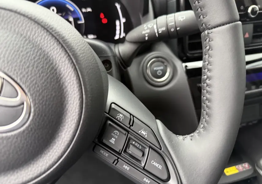 Gros plan sur le volant noir de la Toyota Yaris Cross 130 CH Design 2025, montrant les commandes de régulateur de vitesse.