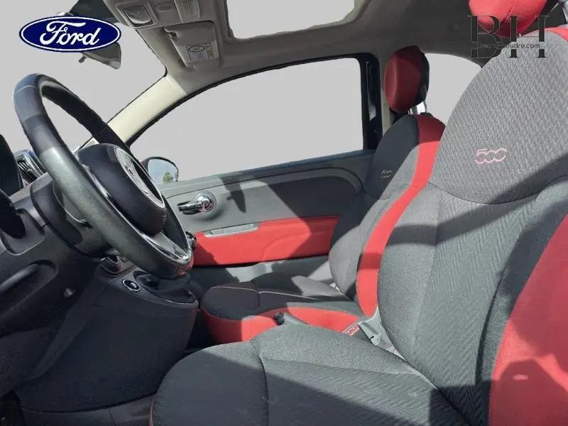 Vue intérieure côté conducteur de la Fiat 500 noire, sièges tissu noir et rouge avec logo 500 brodé, toit ouvrant panoramique visible.