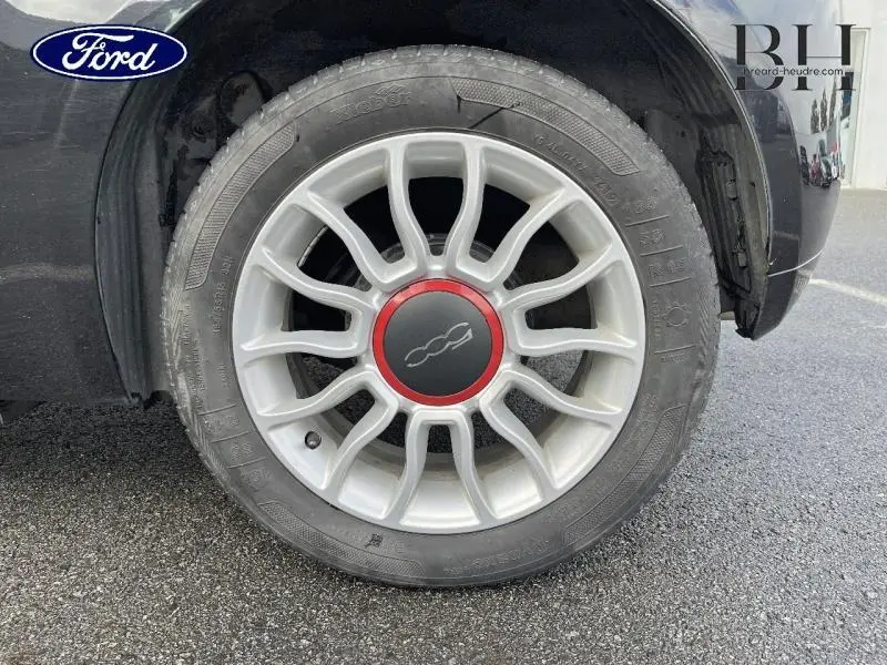 Gros plan sur la roue avant gauche d'une FIAT 500 noire, jante alu avec logo rouge au centre.