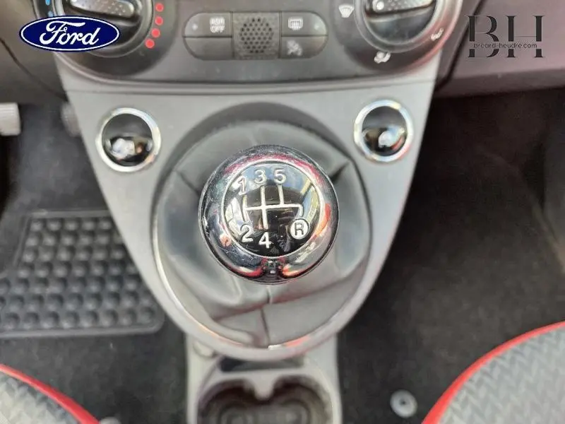 Gros plan sur le levier de vitesses manuel noir de la FIAT 500, entouré de la console centrale grise et sièges avec surpiqûres rouges.