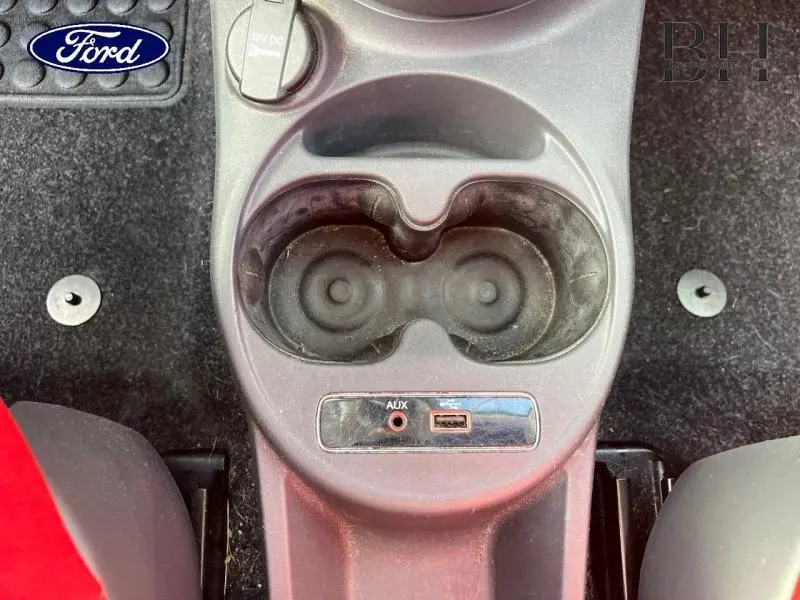 Vue rapprochée de la console centrale avec porte-gobelets et prises AUX/USB d'une Fiat 500 noire, intérieur visible partiellement.
