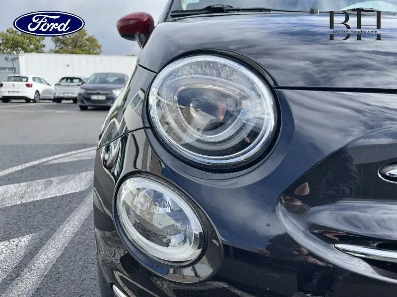 Gros plan sur le phare avant droit d'une Fiat 500 noire, mettant en valeur ses optiques rondes et détails chromés.