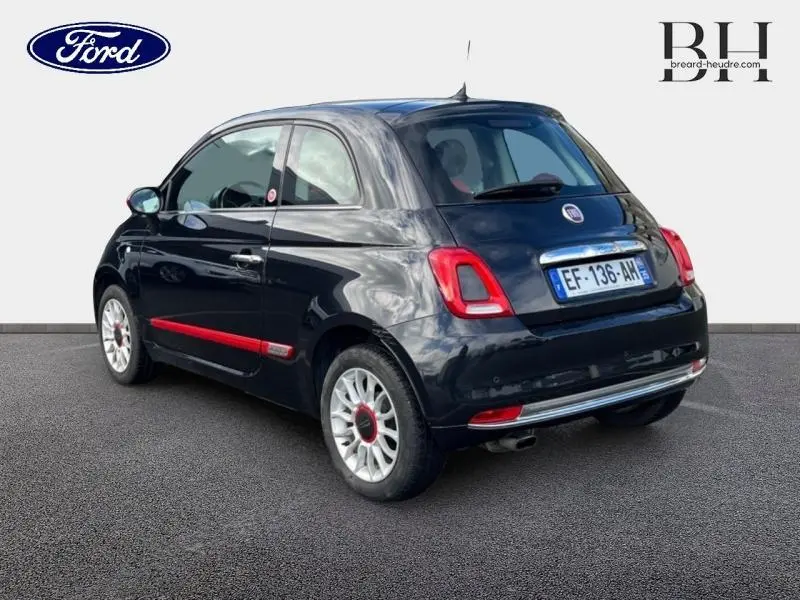 Vue 3/4 arrière droite d'une Fiat 500 noire avec bande rouge latérale et jantes alu au design spécifique.