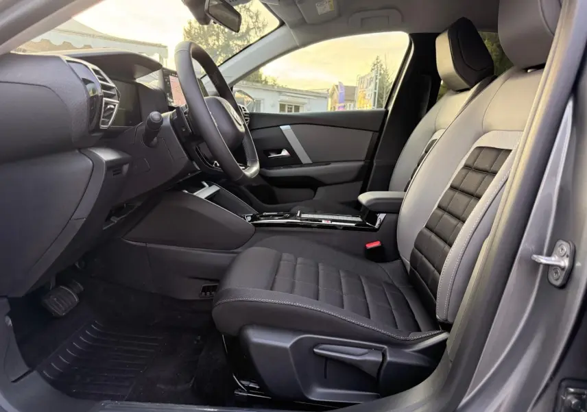 Vue intérieure côté conducteur du Citroën C4 hybride 2025 gris Mercury, mettant en valeur les sièges bi-ton et le tableau de bord moderne.