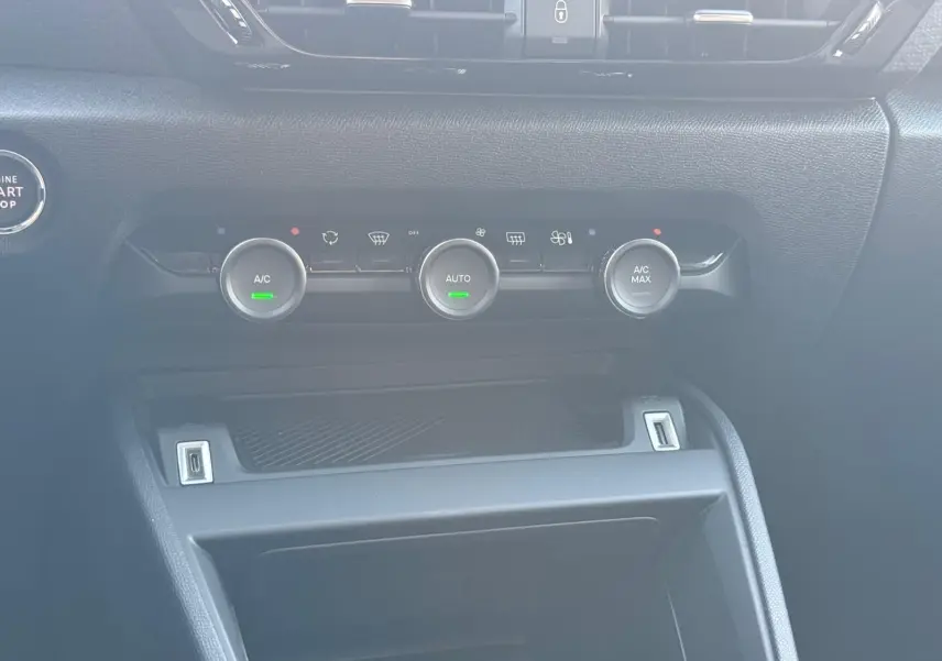 Gros plan sur la console centrale noire du Citroën C4 hybride 2025, avec commandes de climatisation et bouton start/stop.