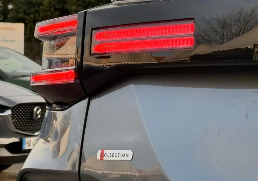 Gros plan sur le feu arrière droit rouge vif et l’insigne Collection d’une Citroën C4 hybride gris Mercury.