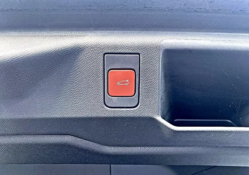 Bouton rouge d'ouverture électrique du coffre sur la garniture intérieure noire d'un Peugeot 5008 Hybrid 145 GT e-dcs6.