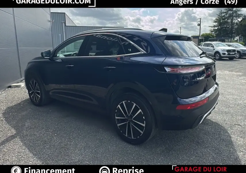 Vue 3/4 arrière droite d'un DS7 bleu saphir avec jantes alliage noires et vitres teintées sur parking extérieur.