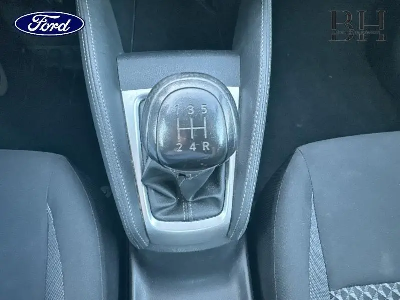 Le levier de vitesses manuel noir vu de dessus entre deux sièges en tissu noir dans l'habitacle d'une Nissan Micra gris acier.