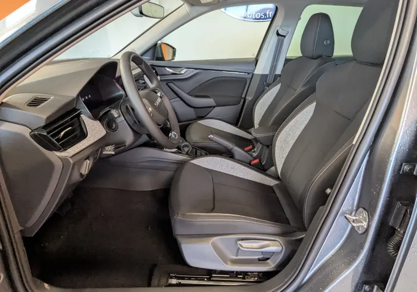 Vue intérieure côté conducteur du Skoda Kamiq gris graphite 2025, sièges tissu noir et gris avec volant multifonction.