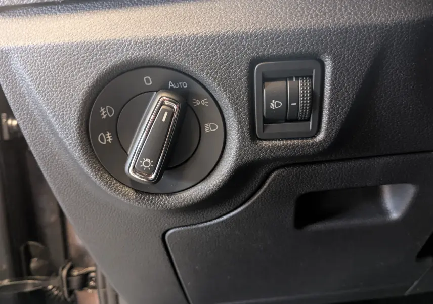 Gros plan sur le bouton de commande des phares et le réglage de hauteur d’éclairage dans l’habitacle noir du Skoda Kamiq 2025.