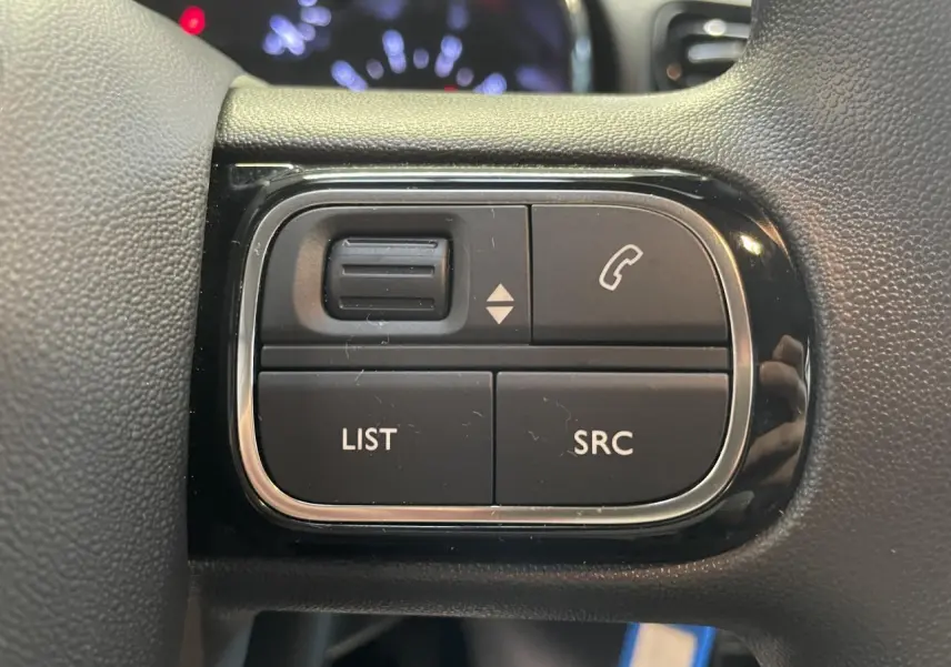 Gros plan sur les commandes audio au volant noir brillant de la Citroën C3 2024, boutons LIST et SRC visibles.