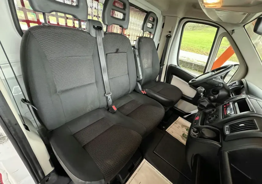 Vue intérieure côté conducteur du Citroën Jumper Benne 2019, sièges tissu noir et tableau de bord avec boîte manuelle.