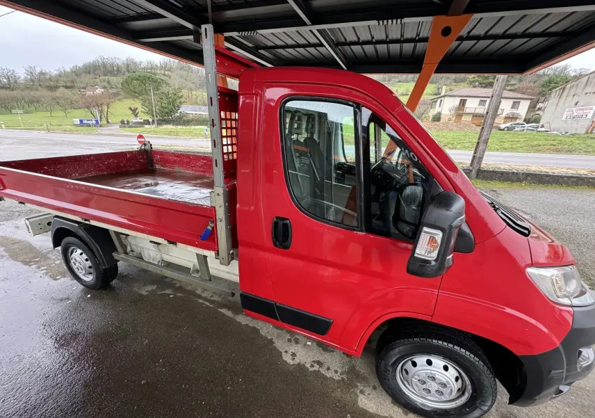 Vue latérale droite d'un Citroën Jumper benne rouge 2019 avec ridelles métalliques et jantes 15 pouces sous abri.