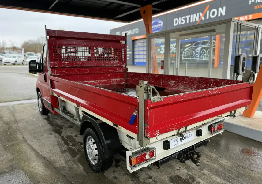 Vue 3/4 arrière droite du Citroën Jumper benne rouge avec ridelles métalliques et attelage visible sous la benne.