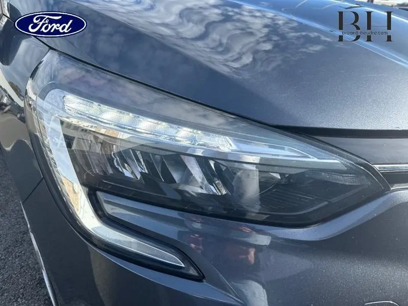 Gros plan sur le phare avant droit gris titanium d'une Renault Clio hybride 2021, soulignant ses feux LED modernes.