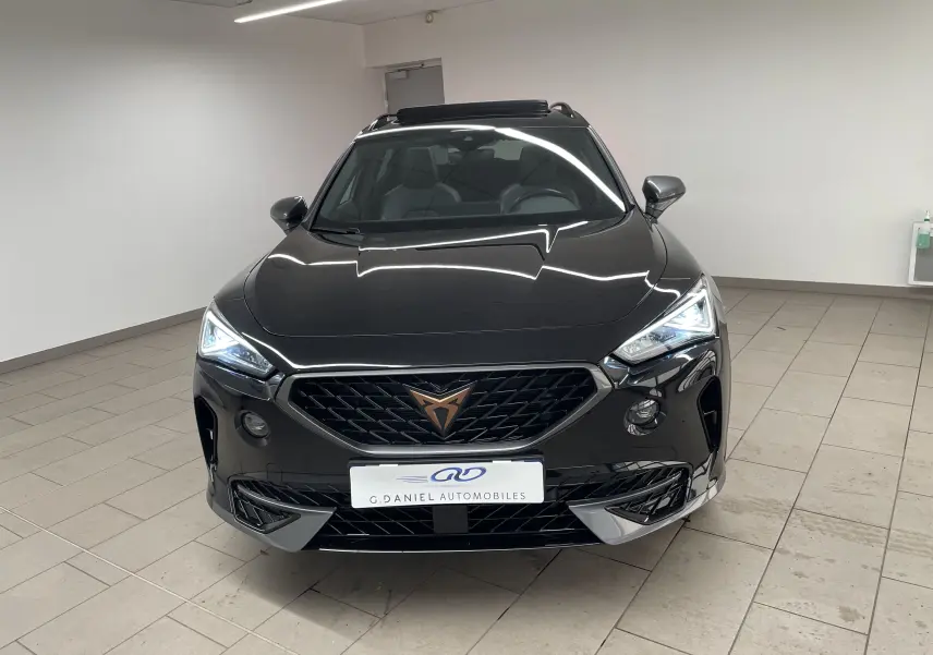 Vue frontale d'un CUPRA Formentor 1.5 TSI 150 DSG7 VZ-LINE noir minuit avec calandre distinctive et phares allumés.