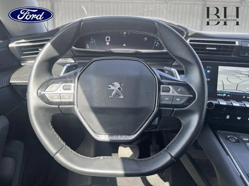 Volant cuir noir au design hexagonal avec logo Peugeot, tableau de bord numérique et écran tactile de navigation visible.