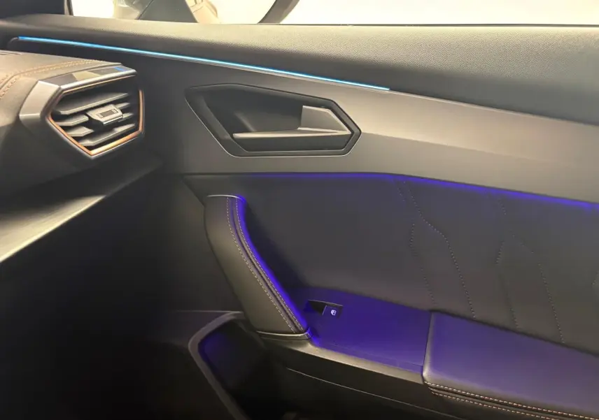 Intérieur côté passager du CUPRA Formentor 2023, montrant la porte avec éclairage d'ambiance bleu et surpiqûres marron.