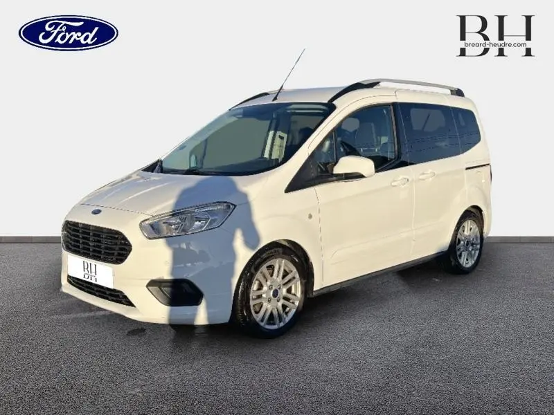 Ford Tourneo Courier blanc glacier en 3/4 avant droit, avec jantes alu et barres de toit visibles.