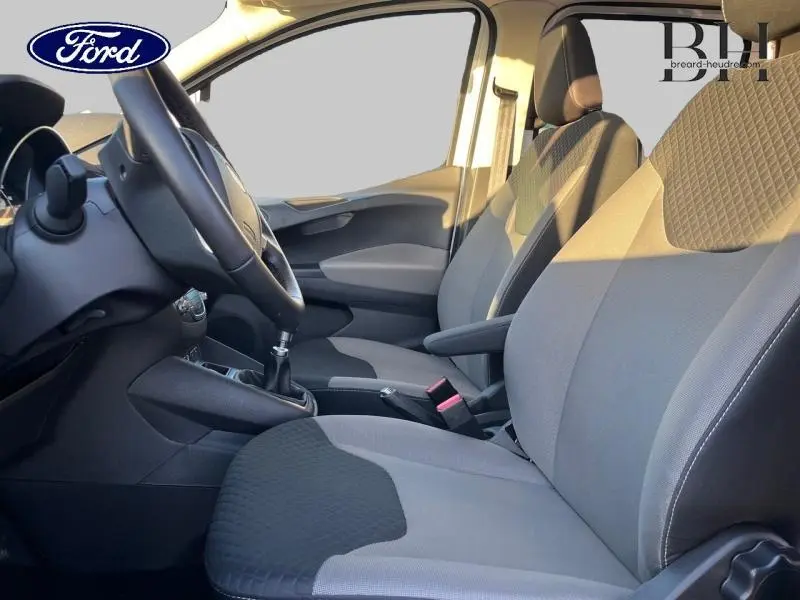 Vue intérieure côté conducteur du Ford Tourneo Courier 2022, sièges gris et volant cuir avec levier de vitesses manuel.