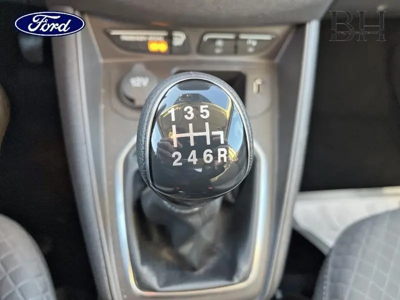 Gros plan sur le pommeau de levier de vitesses manuel noir du Ford Tourneo Courier blanc, avec marquages des six rapports et marche arrière.