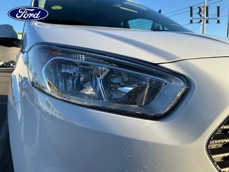 Gros plan sur le phare avant droit du Ford Tourneo Courier blanc Glacier, mettant en valeur la calandre chromée.