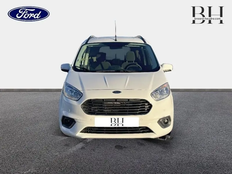 Vue avant du Ford Tourneo Courier blanc Glacier 2022 avec calandre chromée et phares halogènes allumés.