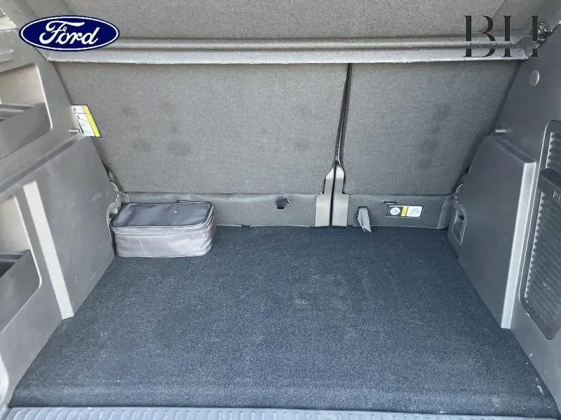 Coffre spacieux du Ford Tourneo Courier blanc, vue intérieure arrière avec tapis noir et rangement latéral.