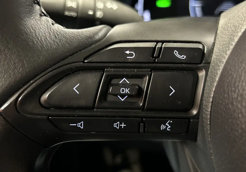 Gros plan sur les commandes au volant noir de la Toyota Yaris Cross 2025, avec boutons de navigation et volume.